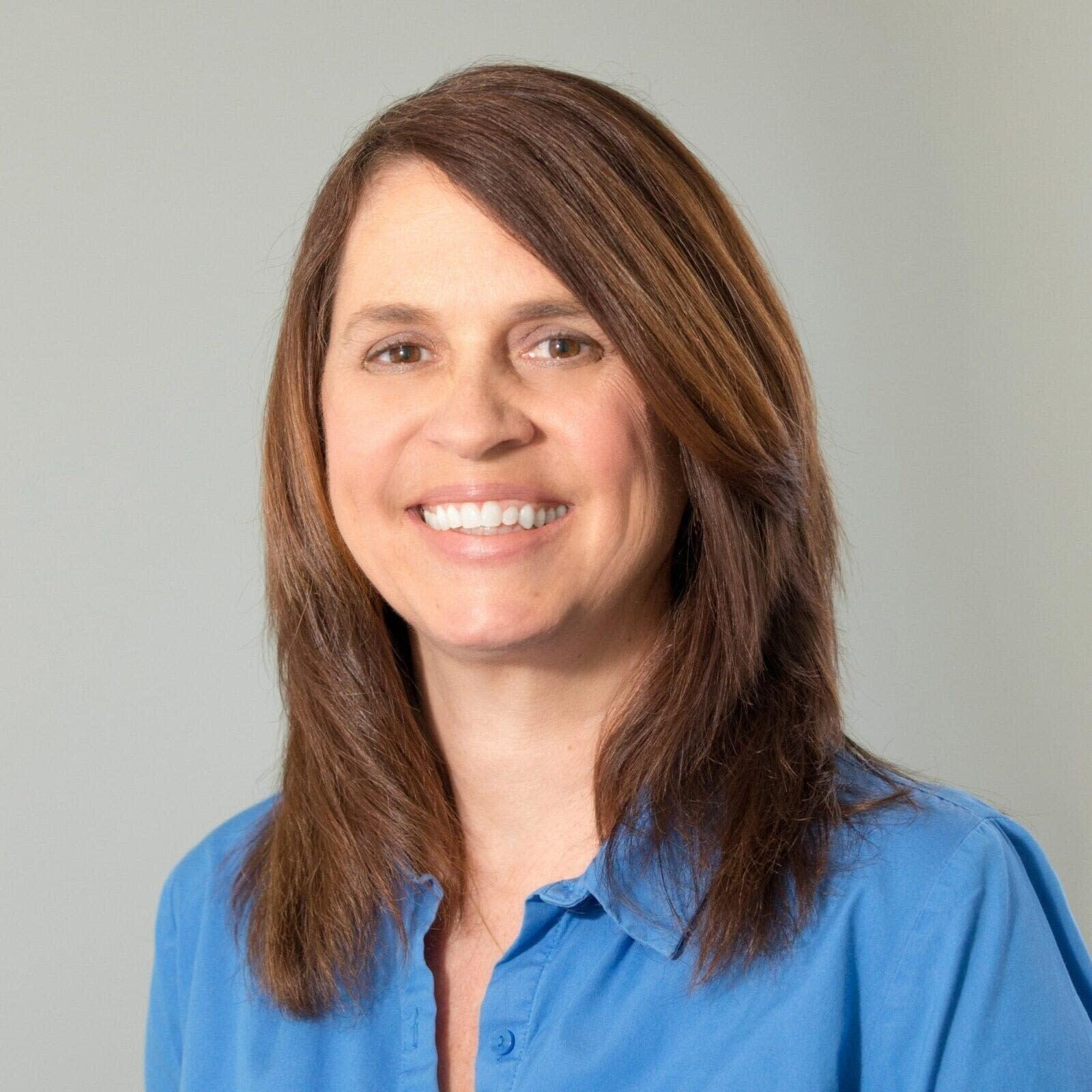 A smiling with long brown hair in blue apparel