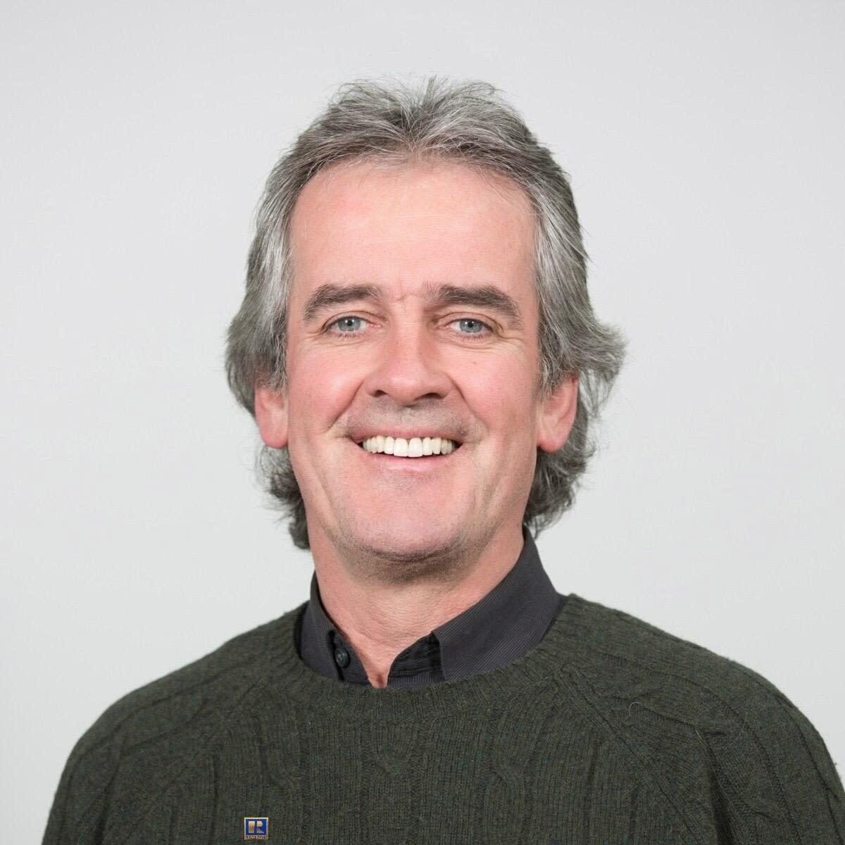 A smiling man with graying hair wearing a green sweater